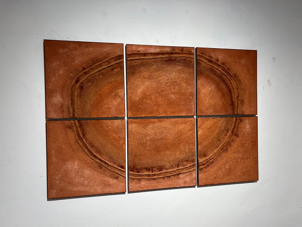 Six square terracotta clay panels by Adam Weismann arranged in a 3x2 grid on a white gallery wall. A pressed elliptical form spans all six panels, evoking an aerial landscape or geological cross-section. Claymoon Studio, Matiz Gallery London.