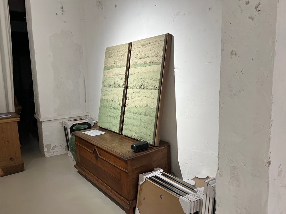 Close detail of two rammed earth clay panels by Adam Weismann, showing horizontal bands of compacted green and grey mineral clay. Raw timber-edged frames visible. Matiz Gallery, London.
