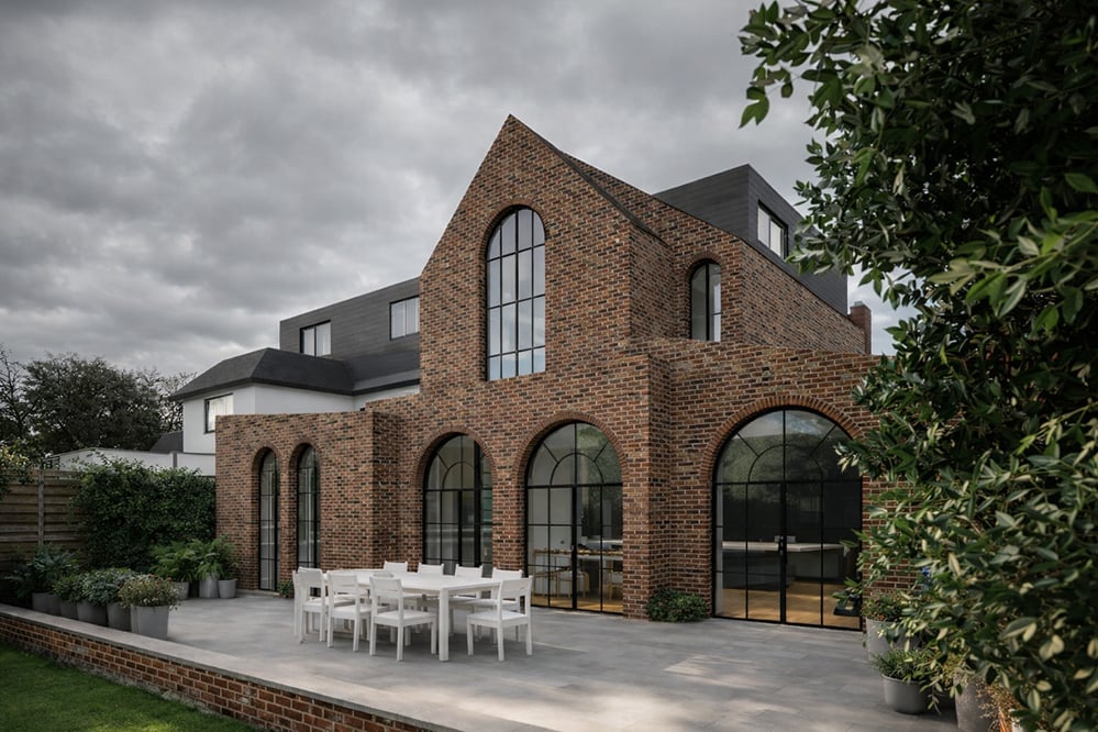 Angled view of a contemporary brick house extension in West Hampstead with arched windows, deep masonry reveals, and garden terrace designed by RISE Design Studio.
