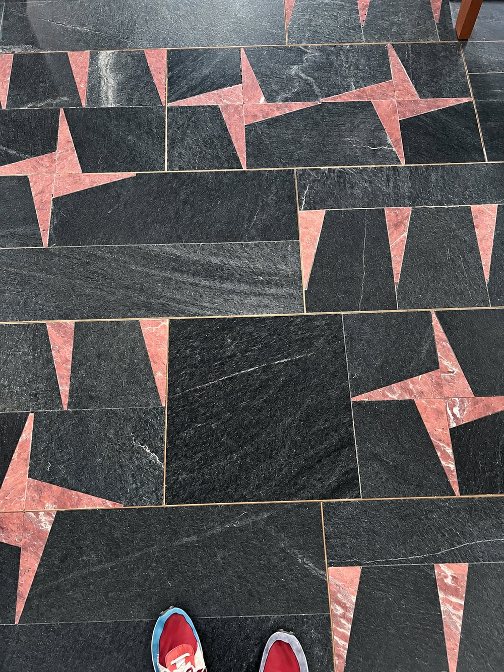 Floor of the Chiesa del Gesù Redentore, Turin, seen from above: black stone slabs with small pink marble triangles set at the joints, and a visitor's red trainers at the bottom edge of the frame. RISE Design Studio.