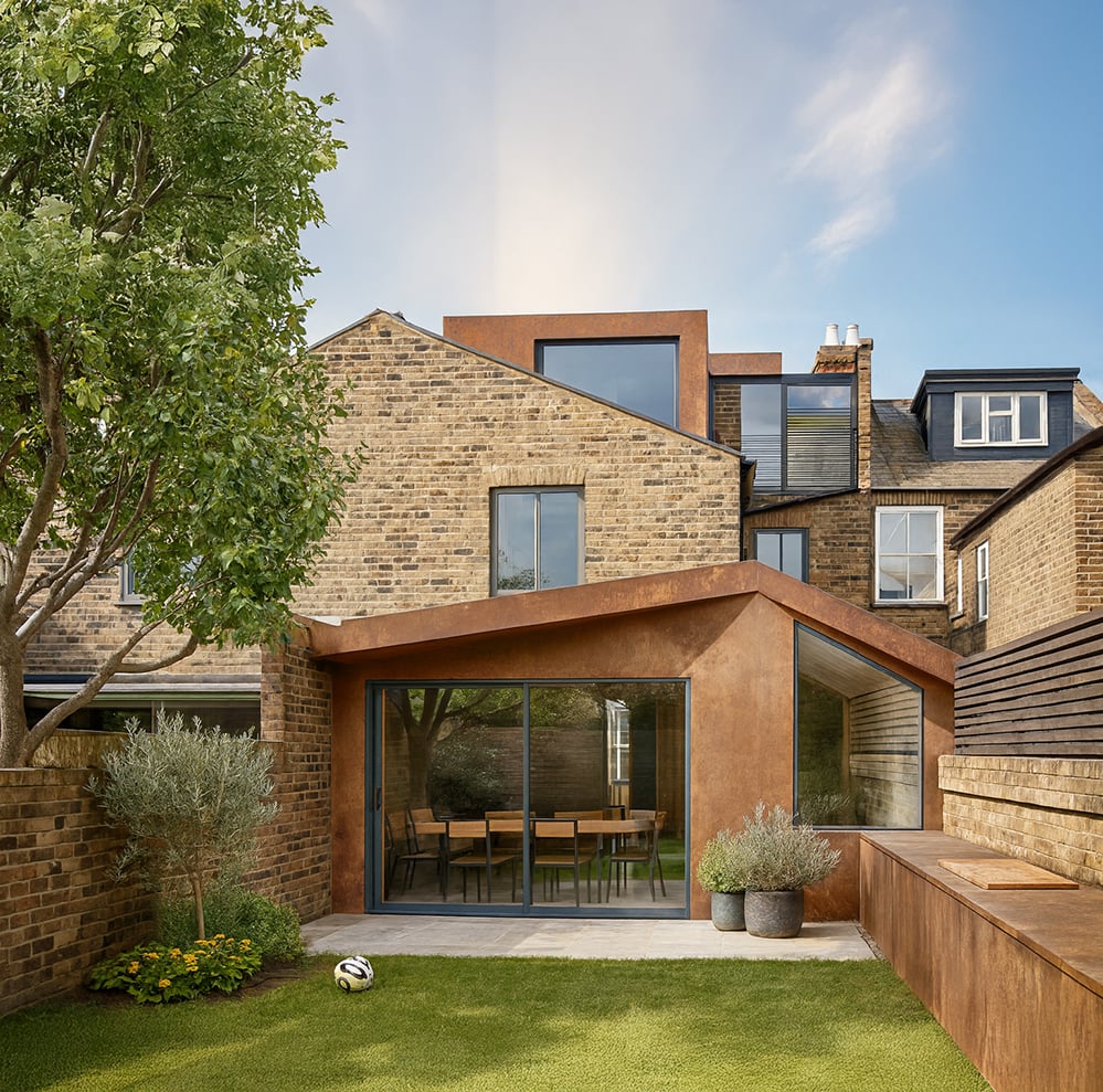 Rear elevation of Corten House featuring the warm-toned Corten extension, large sliding doors, landscaped garden and layered roofline created as part of the low energy retrofit in Kensal Rise.