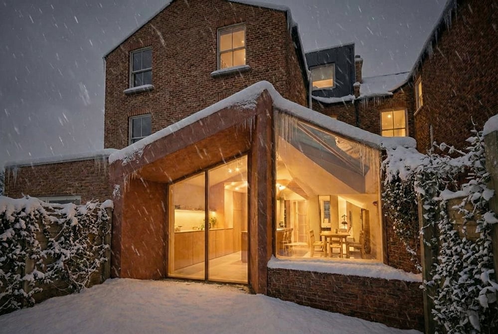 Low-energy residential extension designed by RISE Design Studio, glowing warmly in winter snow, demonstrating strong heat retention, airtight construction, and sustainable fabric-first design that reduces energy demand and improves comfort.