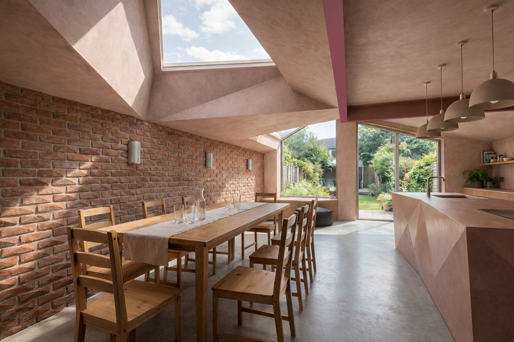Low-energy kitchen and dining extension within a Victorian house in London, with exposed brickwork, folded ceiling geometry, rooflights and fabric-first retrofit design.