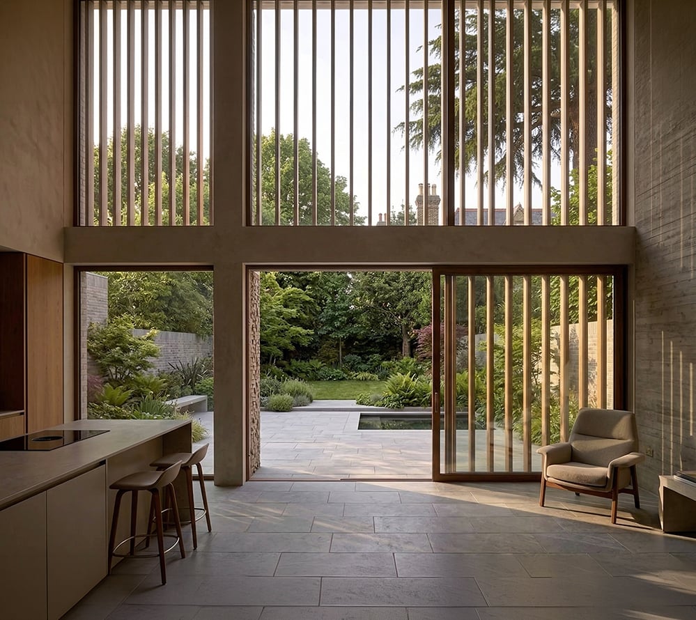 Hampstead House new build interior North London, double-height kitchen living space with timber louvres, sliding glazed doors to stone terrace and mature garden, bespoke joinery and stone floor.