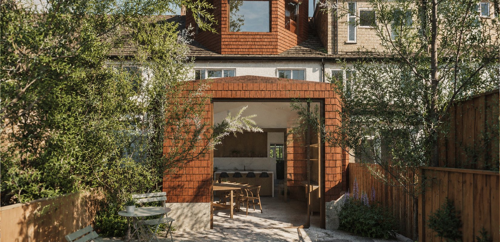 Red clay tiles rear extension to a North London semi-detached house with arched opening, full-width glazing, timber dining table visible inside, and mature olive trees and planted garden in the foreground.