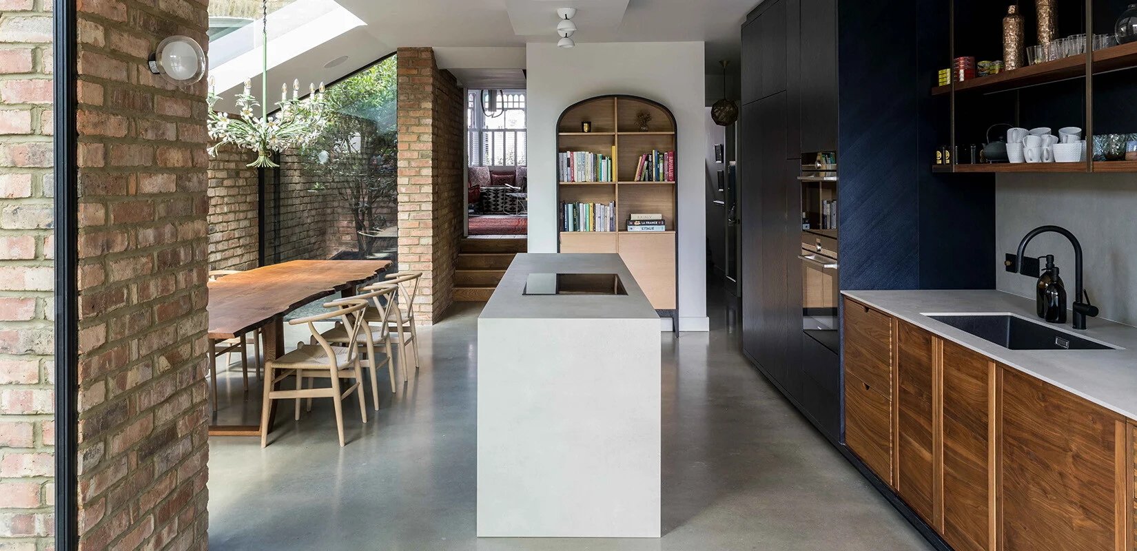 Contemporary low-energy home interior designed by RISE Design Studio featuring exposed brick walls, bespoke timber cabinetry, polished concrete flooring, rooflight and minimalist kitchen detailing within a sustainable London renovation project