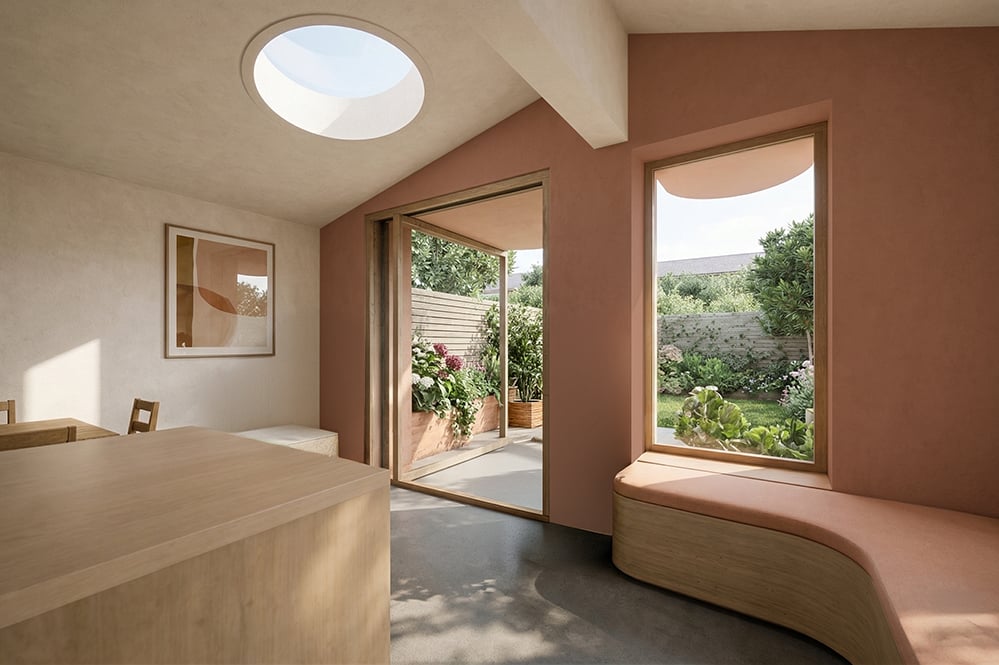 Interior of Scallop House kitchen and dining extension in Stoke Newington - circular rooflight, curved oak window seat, sliding garden doors and pink render walls.