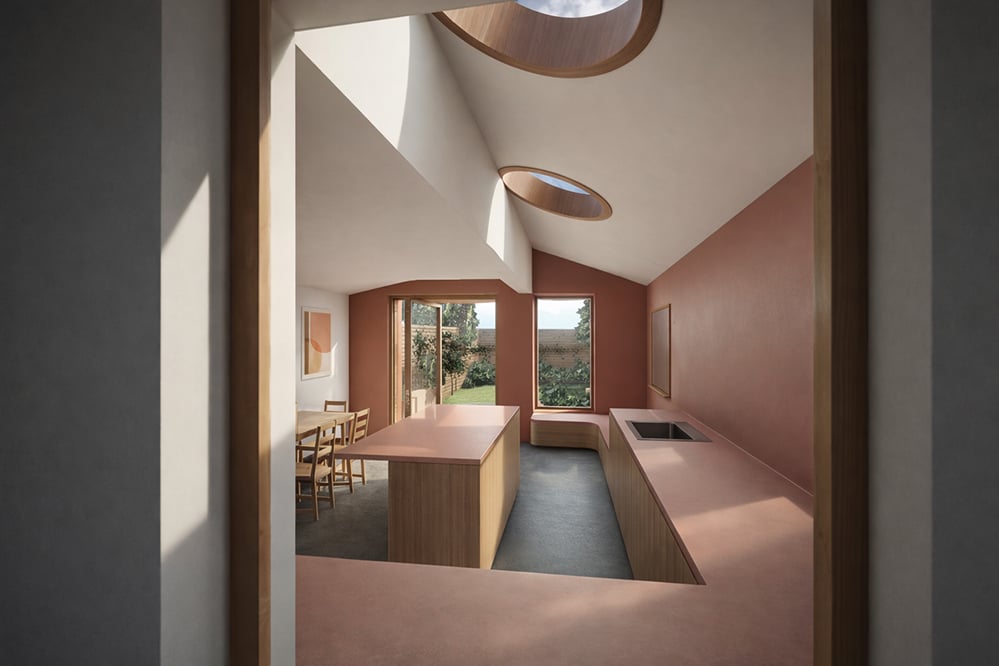 Vaulted kitchen interior at Scallop House Stoke Newington, with two circular rooflights, pink mineral worktop, oak island and garden views. Designed by RISE Design Studio