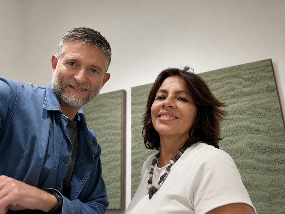 Sean Ronnie Hill, architect and founder of RISE Design Studio, with Ivonne Parra, director of Matiz Gallery London, standing in front of Adam Weismann's green rammed earth panels. May 2026.
