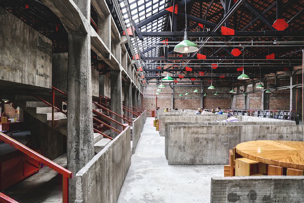Interior view of Sesc Pompeia with exposed concrete structure, red railings and open communal work bays beneath a steel and tile roof. The image highlights Lina Bo Bardi’s approach to social, accessible and sustainable brutalist architecture. Photo by Maria Gonzalez.