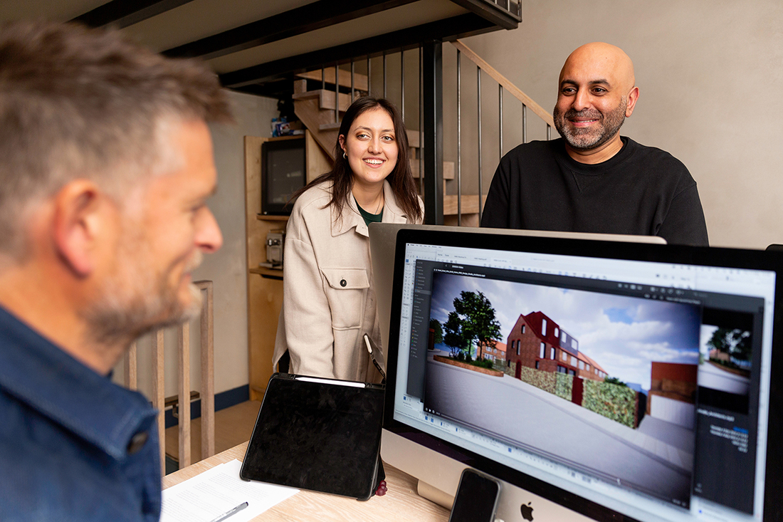 Sean Ronnie Hill and Imran Jahn of RISE Design Studio discussing a sustainable residential project with their team in the studio, with a computer screen showing a 3D design for an energy-efficient London home, reflecting collaboration and low-energy architecture