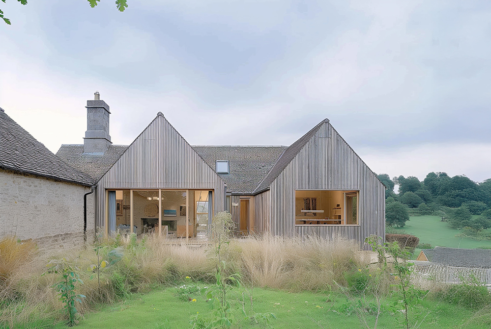 View of a sustainable timber-clad extension to a traditional stone cottage, demonstrating certified Passivhaus principles with large triple-glazed windows, airtight detailing, and low-energy design in a rural English setting.
