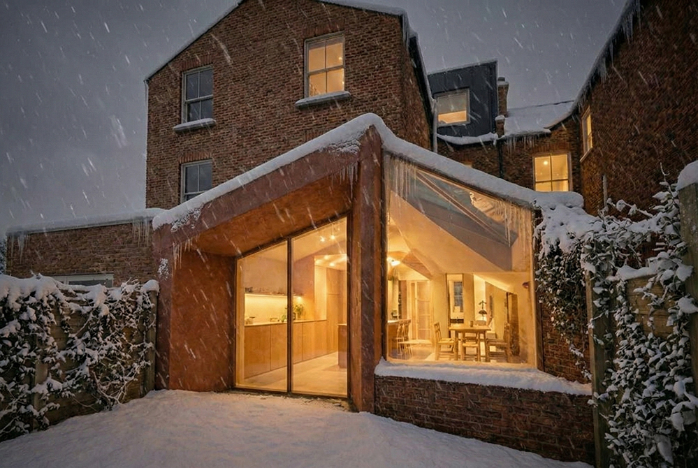 Low-energy residential extension designed by RISE Design Studio, glowing warmly in winter snow, demonstrating strong heat retention, airtight construction, and sustainable fabric-first design that reduces energy demand and improves comfort.