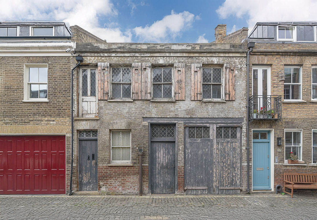 Dilapidated Maida Vale mews house with faded façade and garage door, symbolising the potential of low-energy retrofits to transform London’s historic homes into sustainable dwellings.