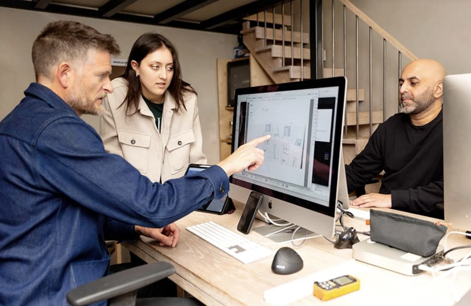 Three architects at RISE Design Studio collaboratively review architectural drawings on screen in a modern studio environment, discussing early-stage planning and sustainable design strategies.