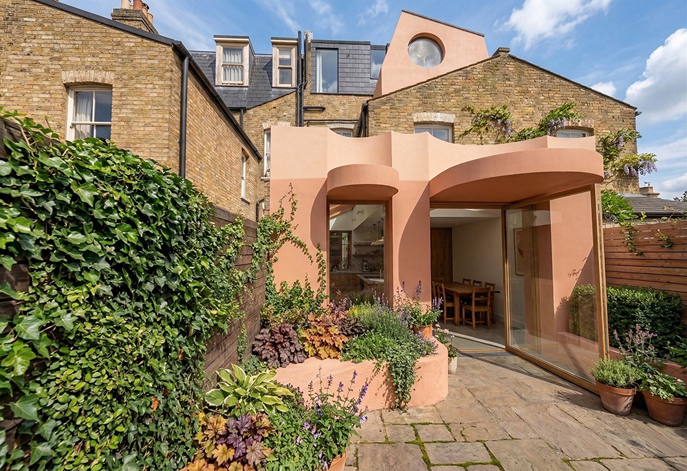Completed pink lime render rear extension to Victorian terrace in Stoke Newington, with curved cylindrical forms and lush garden planting. Designed by RISE Design Studio
