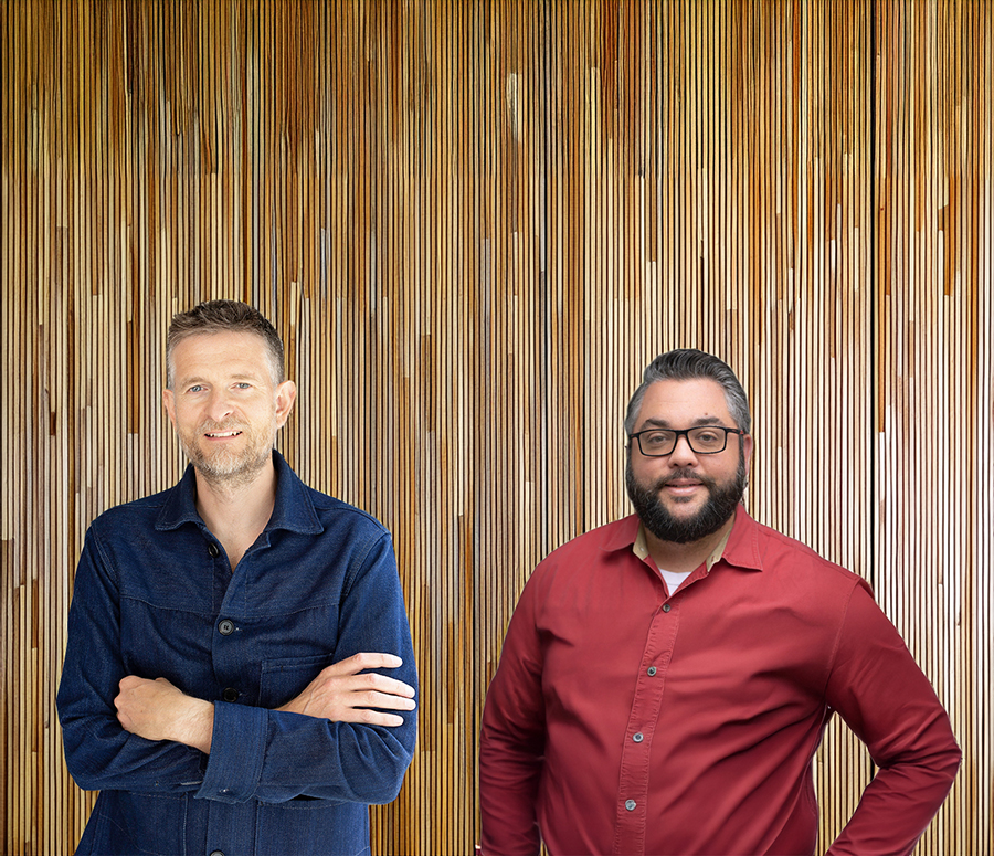 Sean Ronnie Hill, founder of RISE Design Studio, standing alongside Charlie Cicchetti, host of the Green Building Matters podcast, in front of a vertical timber backdrop—capturing their shared commitment to sustainable architecture, natural materials, and regenerative design principles.