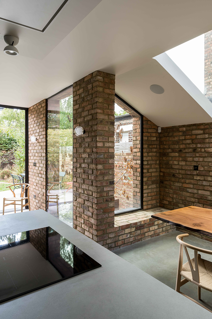 Interior view of Queen’s Park House extension by RISE Design Studio, featuring exposed brick walls, full-height glazing, and a seamless connection to the garden — blending raw materiality with contemporary design in a reimagined Victorian home.